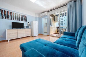 A modern living room with a sofa, a flat-screen TV, a microwave, and a refrigerator.