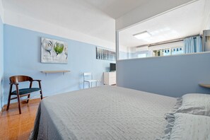A bedroom with a bed, a chair, a desk, and a mirror.