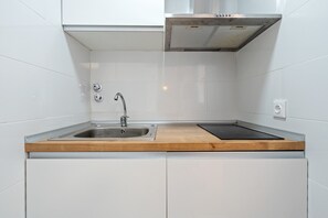 A kitchen with a stainless steel sink, wooden countertop, and white cabinets.