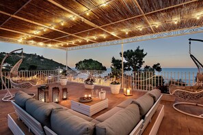 A covered outdoor seating area with a view of the sea, a hanging chair, a sofa, and potted plants. - Apartment 'Rooftopnerano - Amazing Sea View' with Sea View, Wi-Fi and Air Conditioning (Marina del Cantone)
