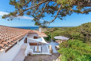 A villa with a tiled roof, outdoor seating, and a view of the sea.