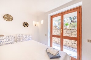 A bedroom with a bed, a window with a stone wall view, and wall-mounted lights.