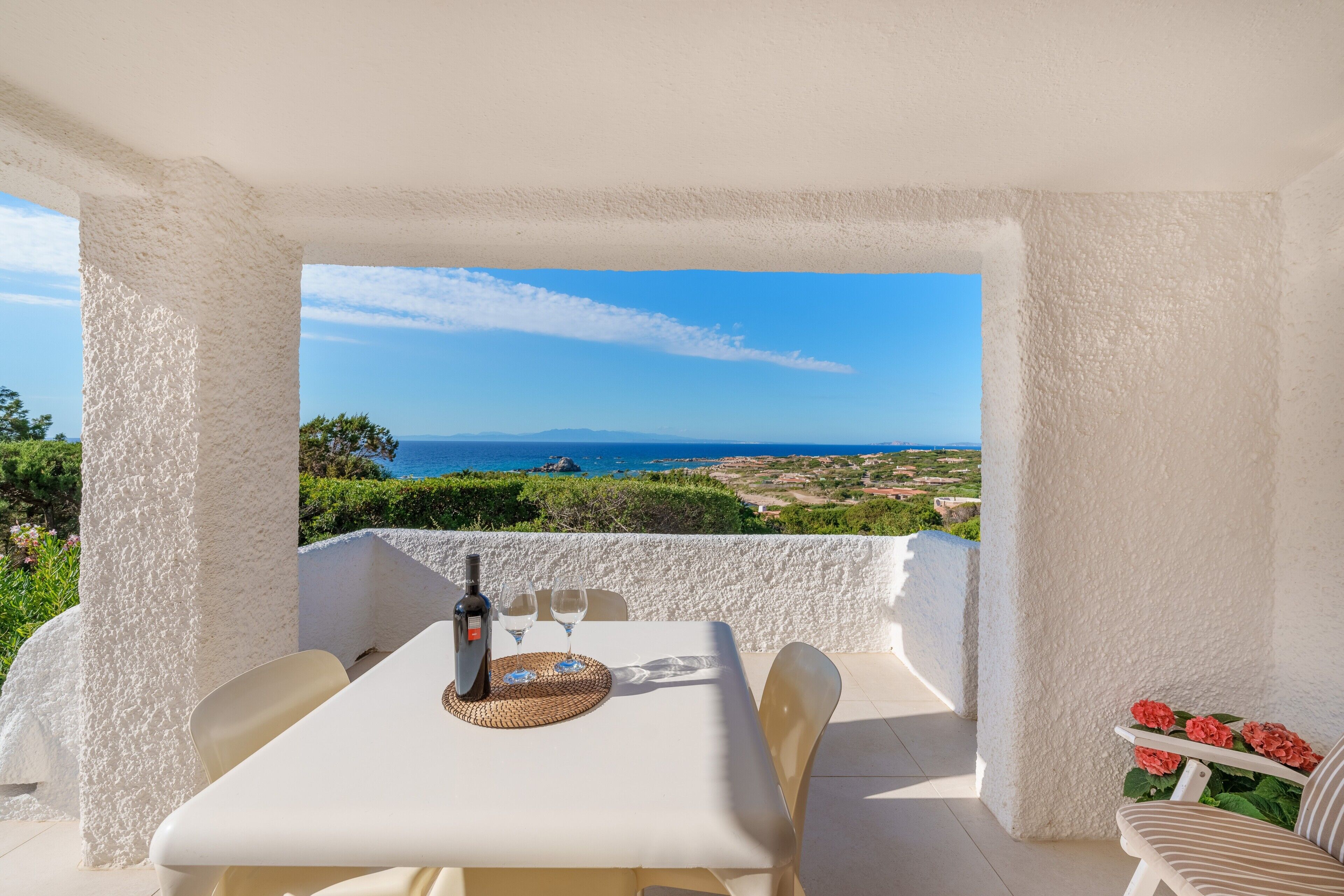 A terrace with a table set for two, a bottle of wine, and a view of the sea.