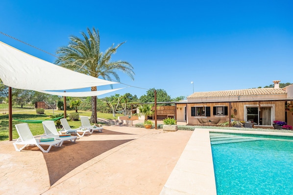 A pool area with lounge chairs, a covered seating area, and a building with a tiled roof.
