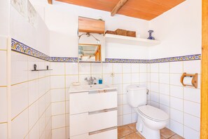 Une salle de bain avec des carreaux blancs, un lavabo, des toilettes et un miroir.
