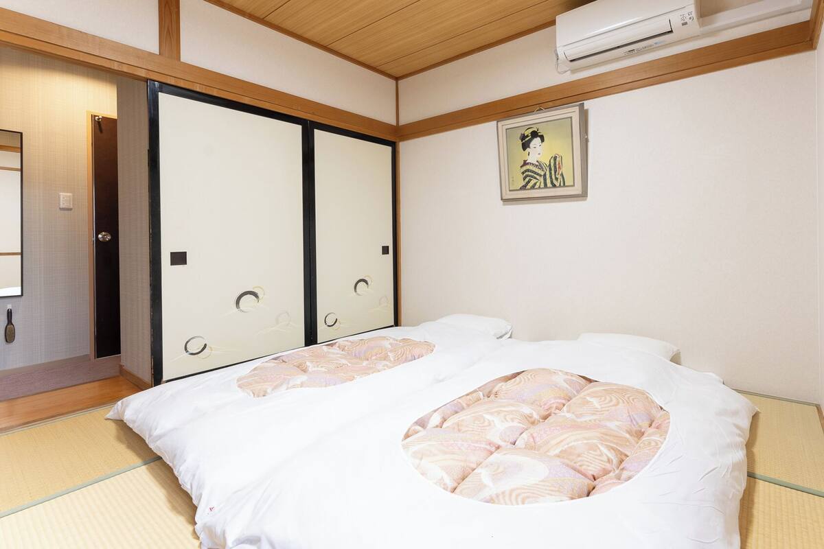 A traditional Japanese room with tatami flooring, a futon bed, sliding doors, and a wall-mounted air conditioner.