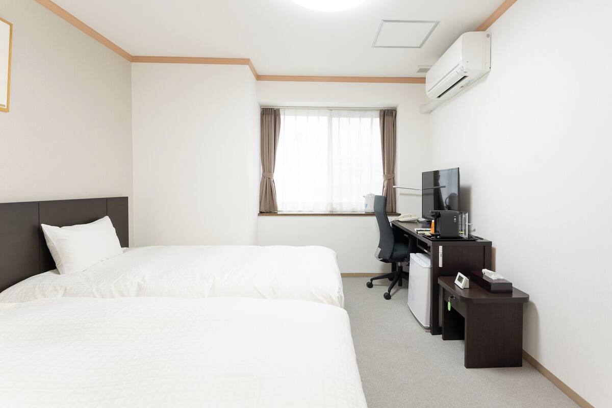 A hotel room with a bed, a desk with a computer, a TV, and an air conditioner.