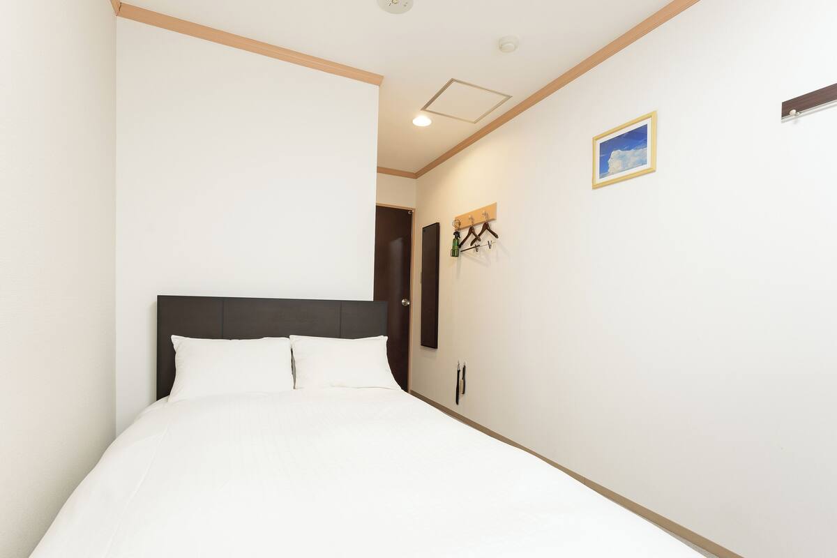 A bedroom with a bed, a door, a coat rack, and a picture on the wall.