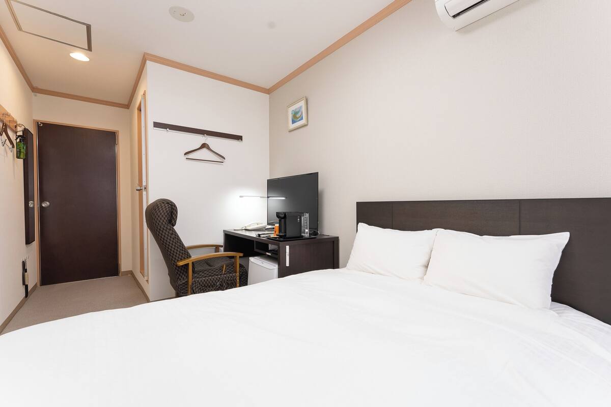 A hotel room with a bed, a desk with a television, a chair, and a wardrobe.