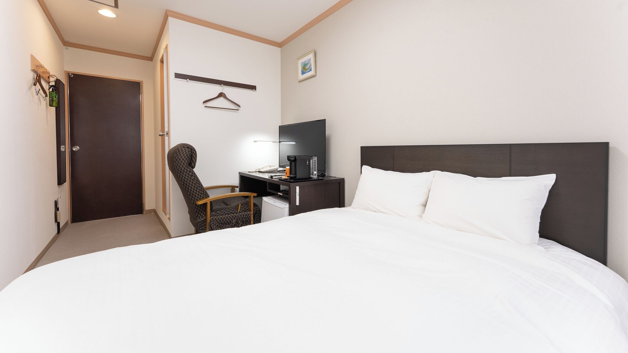 Une chambre d’hôtel avec un lit, un bureau, une chaise, une télévision et une porte.