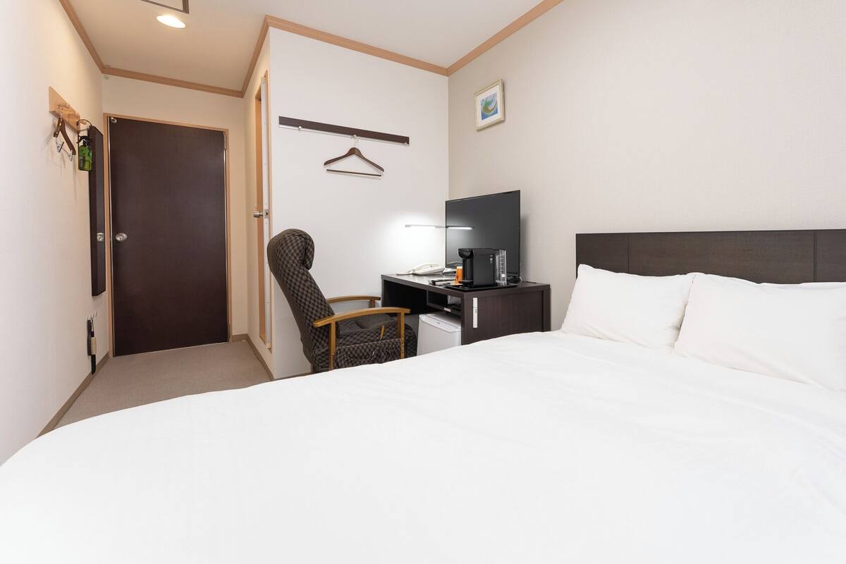 A hotel room with a bed, desk, chair, TV, and a door.