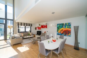 Un salon moderne avec un coin repas, de grandes fenêtres et un tableau aux couleurs vives.