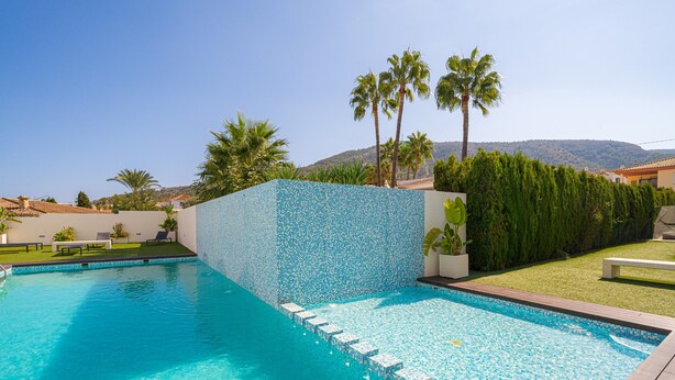 Une piscine avec un mur carrelé, des palmiers et une vue sur les collines.