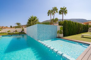 Une piscine avec un mur carrelé, des palmiers et une vue sur les collines.