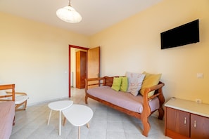Una habitación con un sofá de madera, una pequeña mesa blanca, un televisor montado en la pared y un mueble de madera.