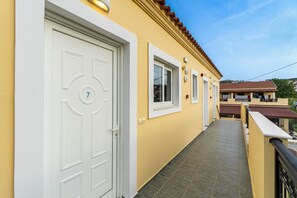 Un edificio amarillo con una puerta blanca numerada con el 7, un balcón con azulejos y un tejado de tejas rojas.