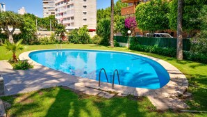 Une piscine à bord incurvé, entourée d’une pelouse bien entretenue et de divers arbres.