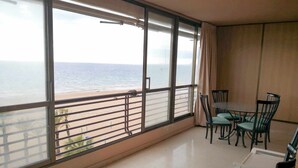 Un balcon avec vue sur la plage et l’océan, une table à manger avec des chaises et une fenêtre avec des rideaux.