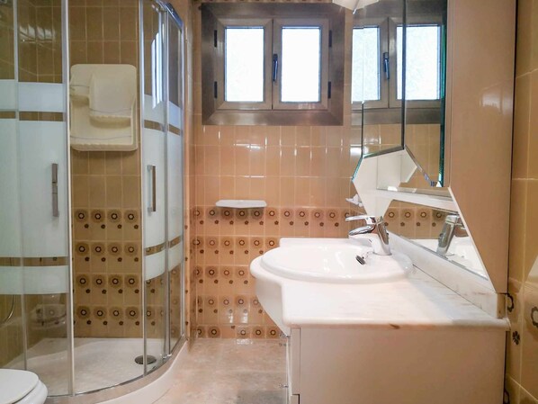Ein Badezimmer mit Duschkabine, Waschbecken mit Spiegel und gemusterten Fliesen.