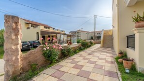 Une rue résidentielle avec un trottoir dallé, un mur en pierre et un immeuble doté d’un balcon et d’une enseigne.