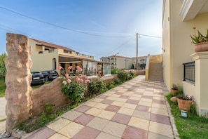 A residential street with a paved walkway, a stone wall, and a building with a balcony and a sign.