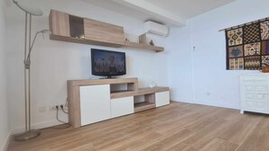 Ein modernes Wohnzimmer mit Flachbildfernseher auf einem Holz-TV-Möbel, einem weißen Schrank und einer Wanddekoration mit Muster.