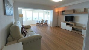 Ein modernes Wohnzimmer mit einer Couch, einem Esstisch mit Stühlen, einem Fernseher auf einer Holzkommode und einem großen Fenster mit Blick.