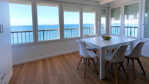 Ein Essbereich mit Meerblick durch große Fenster, ein weißer Tisch und moderne Stühle.