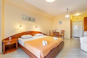 Quarto de hotel com cama, mesas de cabeceira, escrivaninha, cadeiras e uma pequena mesa com um vaso.