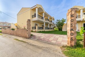 Un hôtel à plusieurs étages doté de balcons, d’une entrée pavée et d’une enseigne en pierre portant le nom « KOSMOS ».