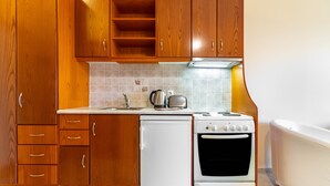 Une cuisine de taille réduite, dotée de meubles en bois, d’un réfrigérateur blanc, d’une cuisinière et d’un dosseret carrelé.