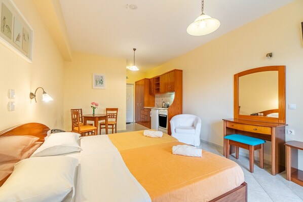 A hotel room with a bed, a desk, a chair, a mirror, and a kitchenette.