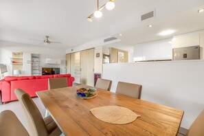 Une cuisine moderne avec des meubles blancs, une table à manger avec des chaises, et un canapé rouge en arrière-plan.