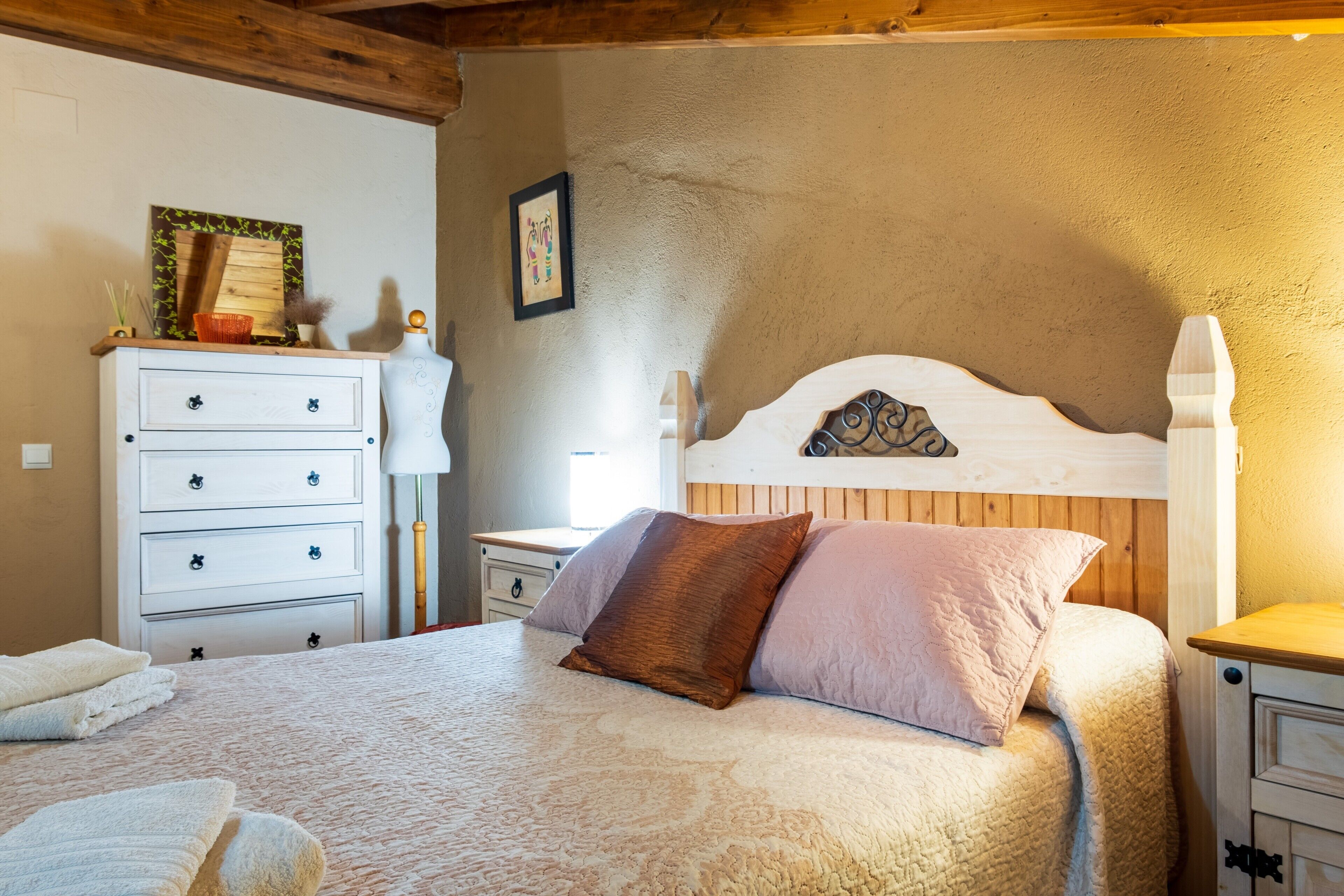 A bedroom with a bed, a dresser, a nightstand, and a wall-mounted shelf.