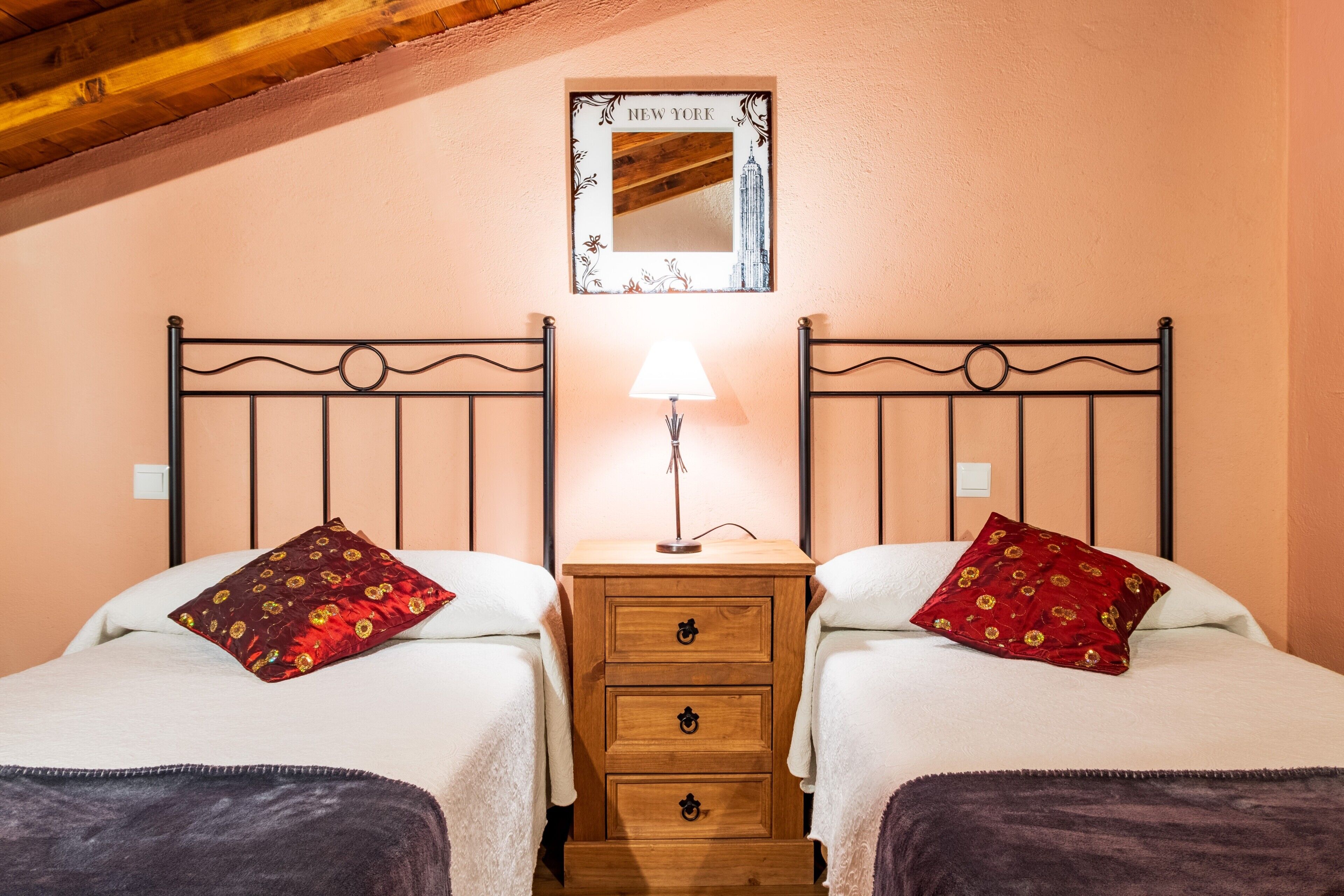 A double bed with two pillows, a nightstand with a lamp, a mirror, and a wooden headboard.
