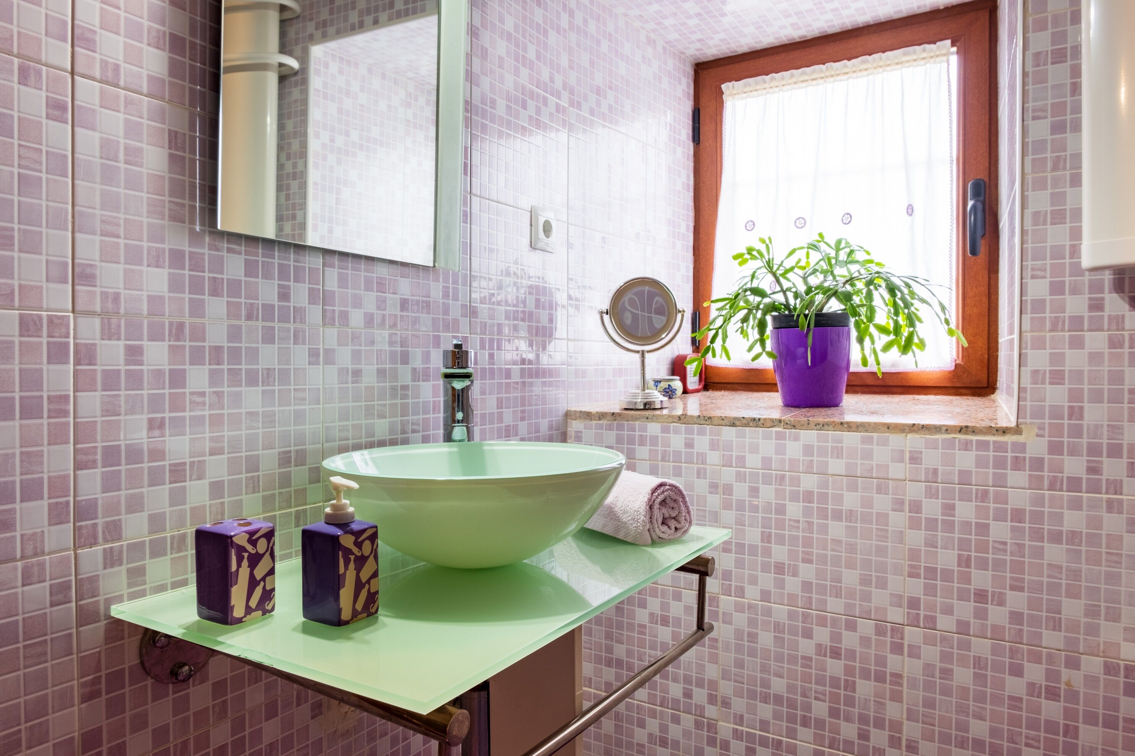 A bathroom with a large green sink, a mirror, a window with a plant, and a tiled wall.