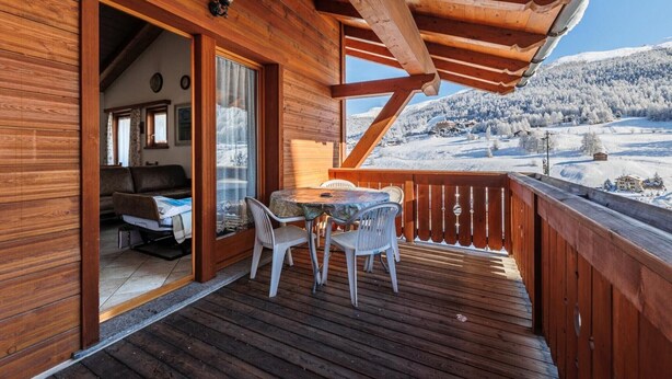 A wooden deck with a table and chairs, a sofa, and a view of a snowy landscape. - Apartment 'Gerry House' with Mountain View, Balcony and Wi-Fi (Livigno)