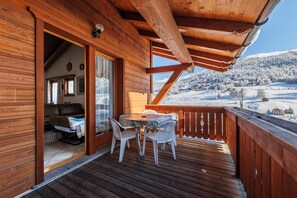 Eine Holzterrasse mit Tisch, Stühlen und einer Couch, mit Blick auf eine verschneite Landschaft.