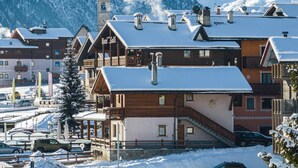 A hotel with a clock tower, wooden architecture, and a snowy mountain backdrop. - Apartment 'Gerry House' with Mountain View, Balcony and Wi-Fi (Livigno)