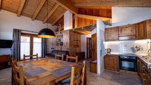 A wooden interior with a dining table, chairs, a sofa, a kitchen area, and a television. - Apartment 'Gerry House' with Mountain View, Balcony and Wi-Fi (Livigno)