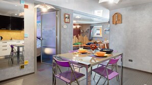A modern dining area with a glass table, purple chairs, and a view into the kitchen. - Apartment 'Maison De La Musique' with Mountain View, Shared Terrace and Wi-Fi (Cogne)