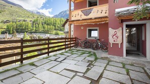A building with a wooden balcony, stone steps, and a mountain view. - Apartment 'Maison De La Musique' with Mountain View, Shared Terrace and Wi-Fi (Cogne)
