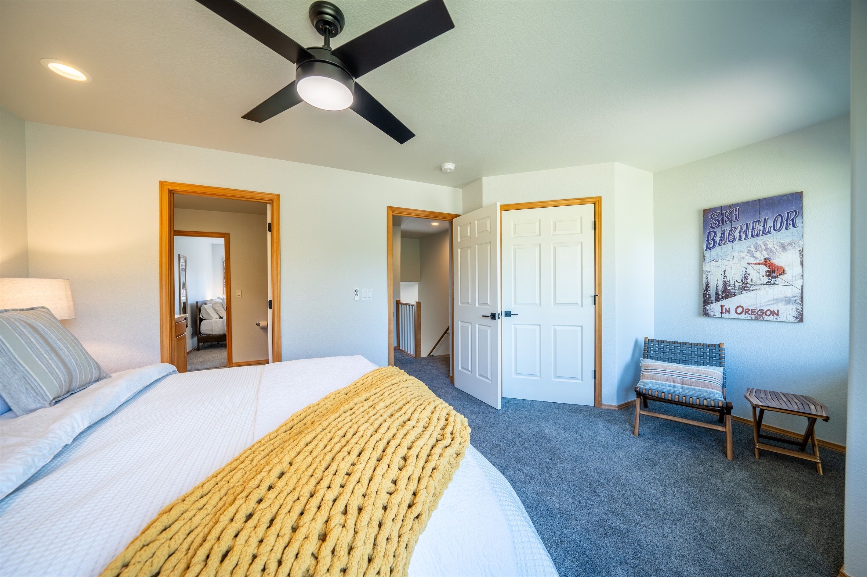 A bedroom with a bed, a ceiling fan, a door, a bench, and a poster on the wall.