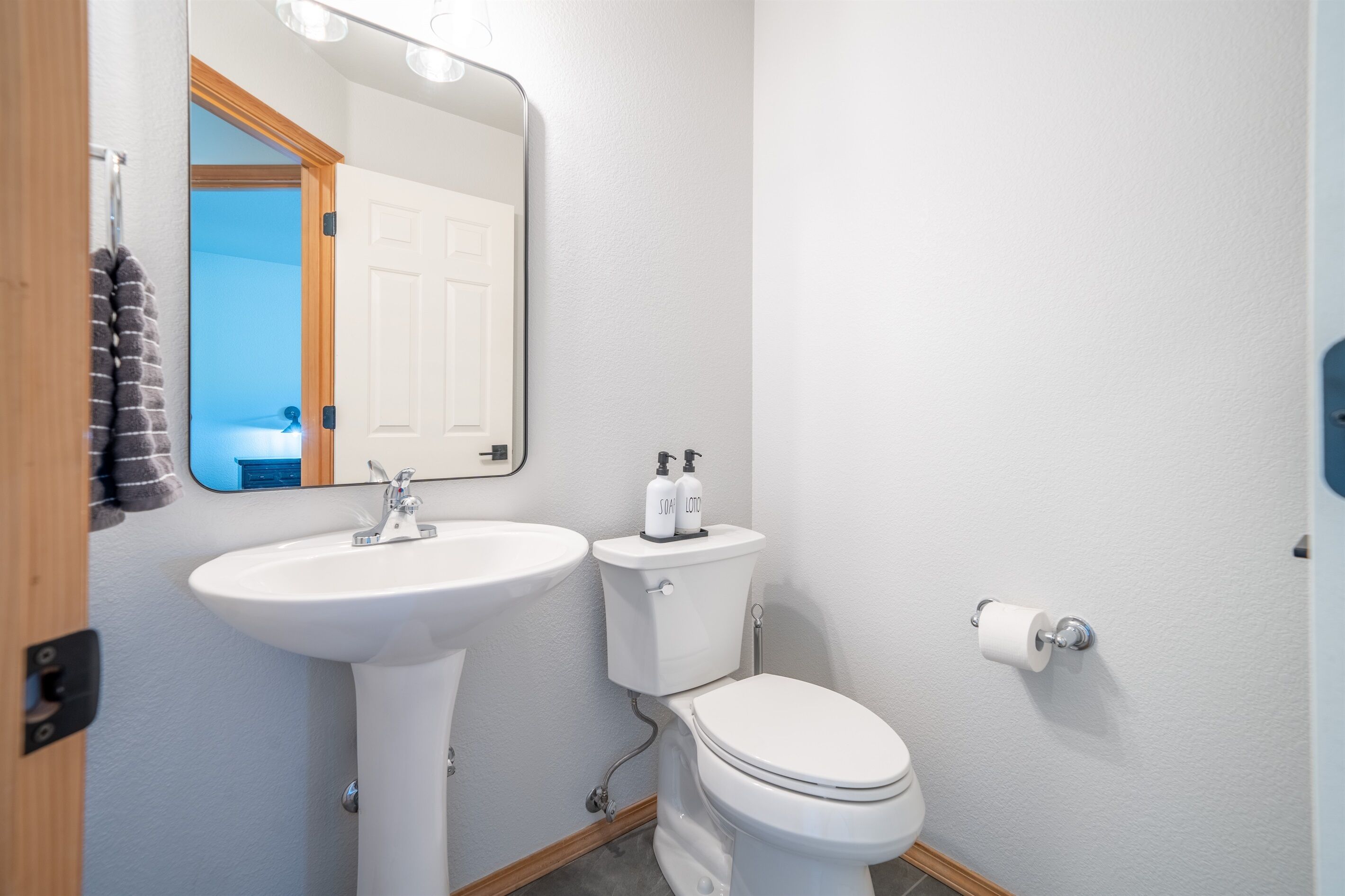 A bathroom with a white sink, toilet, and mirror. There are two bottles of soap on the toilet tank.