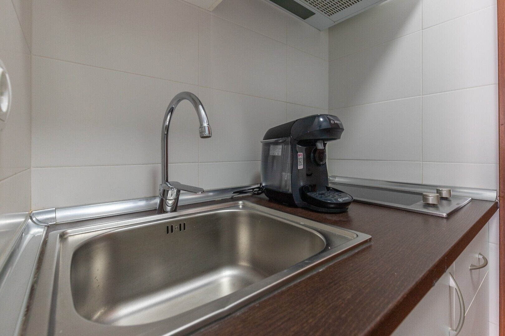 A stainless steel sink with a modern faucet, a black coffee maker, and a wooden countertop.