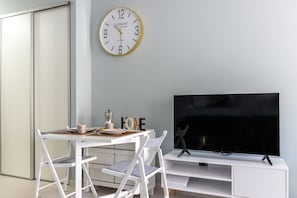 Ein modernes Zimmer mit einem weißen Schreibtisch, zwei Stühlen, einem Fernseher und einer Wanduhr.