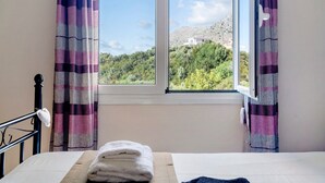 Un dormitorio con cama, ventana con cortinas y vistas a una ladera.