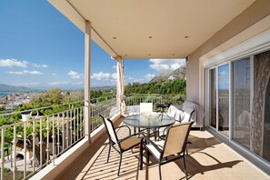 Un balcón con mesa y sillas, vistas de la ciudad y una montaña al fondo.