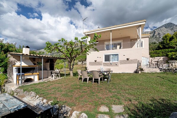 Una casa de dos pisos con un patio, mobiliario exterior y una zona de barbacoa.