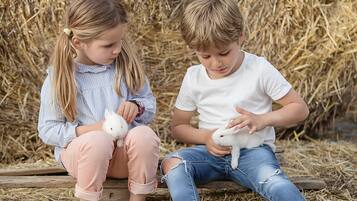 Two children sitting on a wooden bench outdoors with hay in the background.